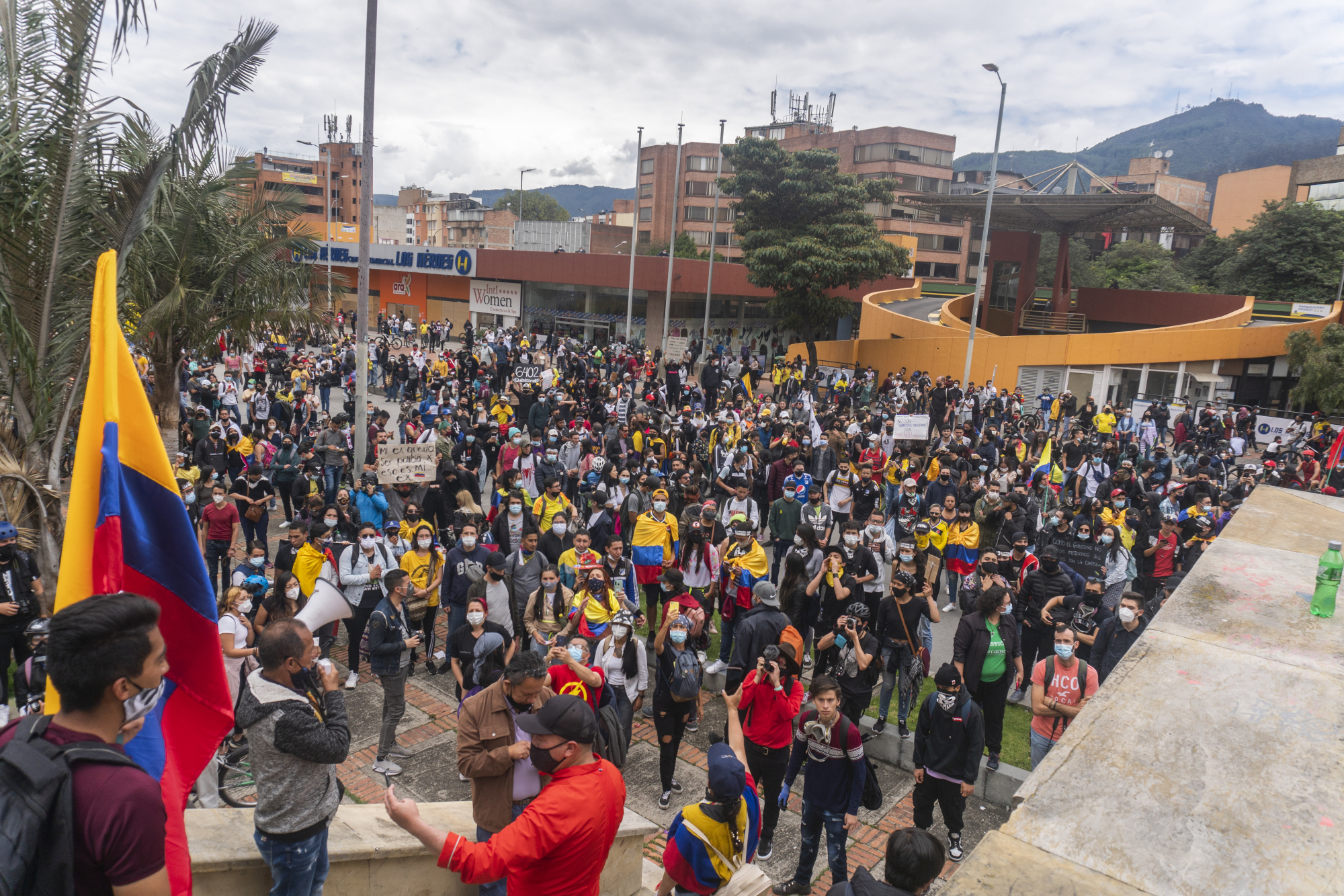 A group of protesters carrying Colombian flags gather in front of a building.
