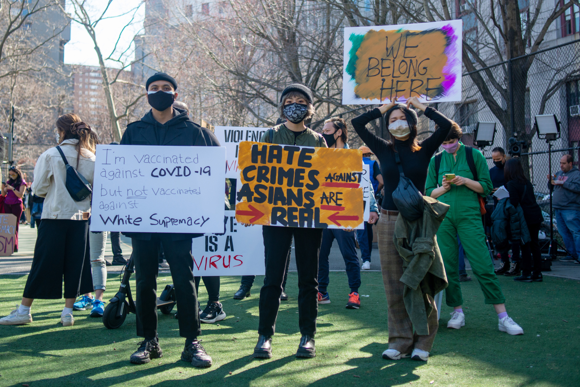 A group of protesters hold various colored signs calling out white supremacy and discrimination against Asian American communities.