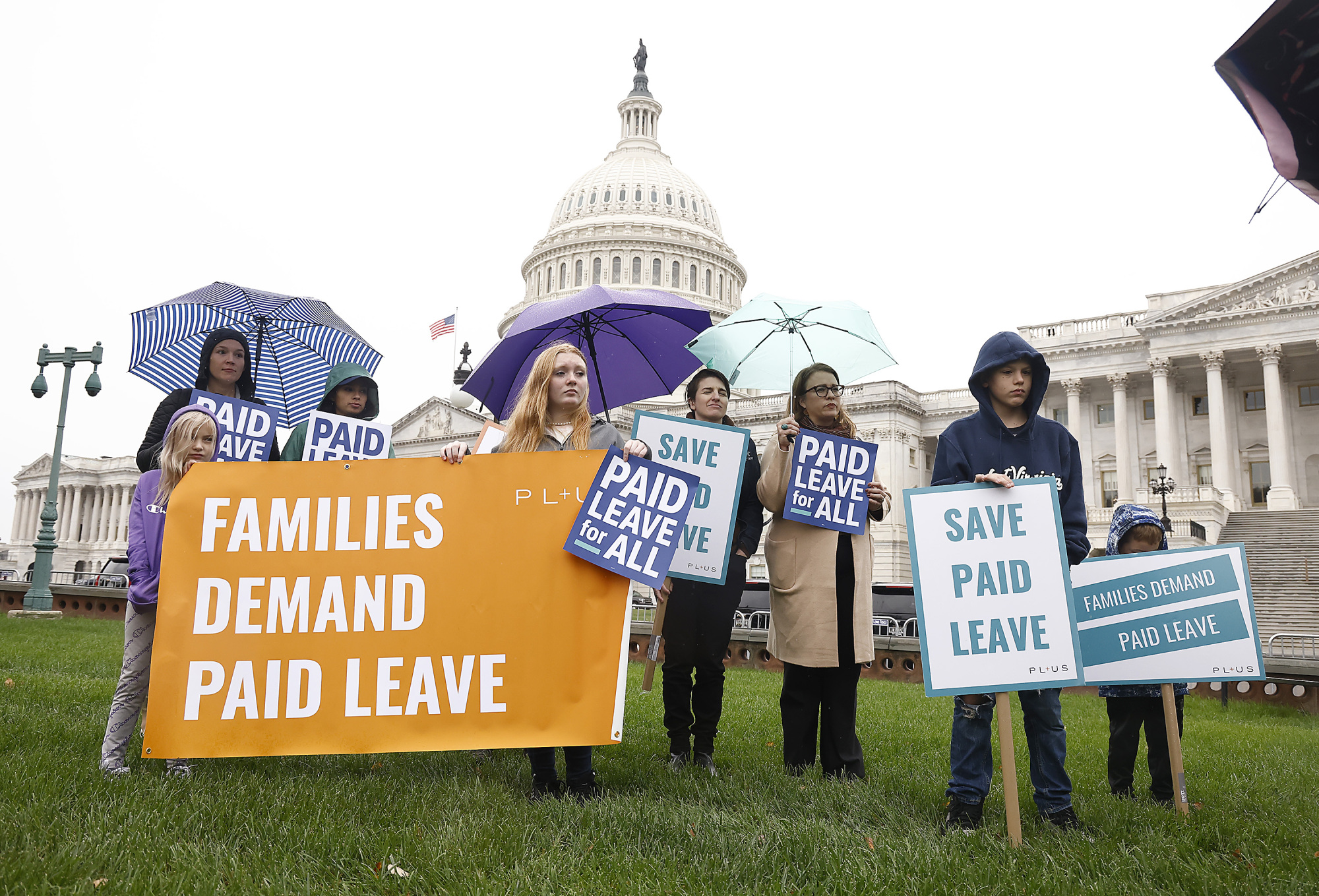 A group of paid leave for all supporters hold large signs in front of the United States Capitol Building.