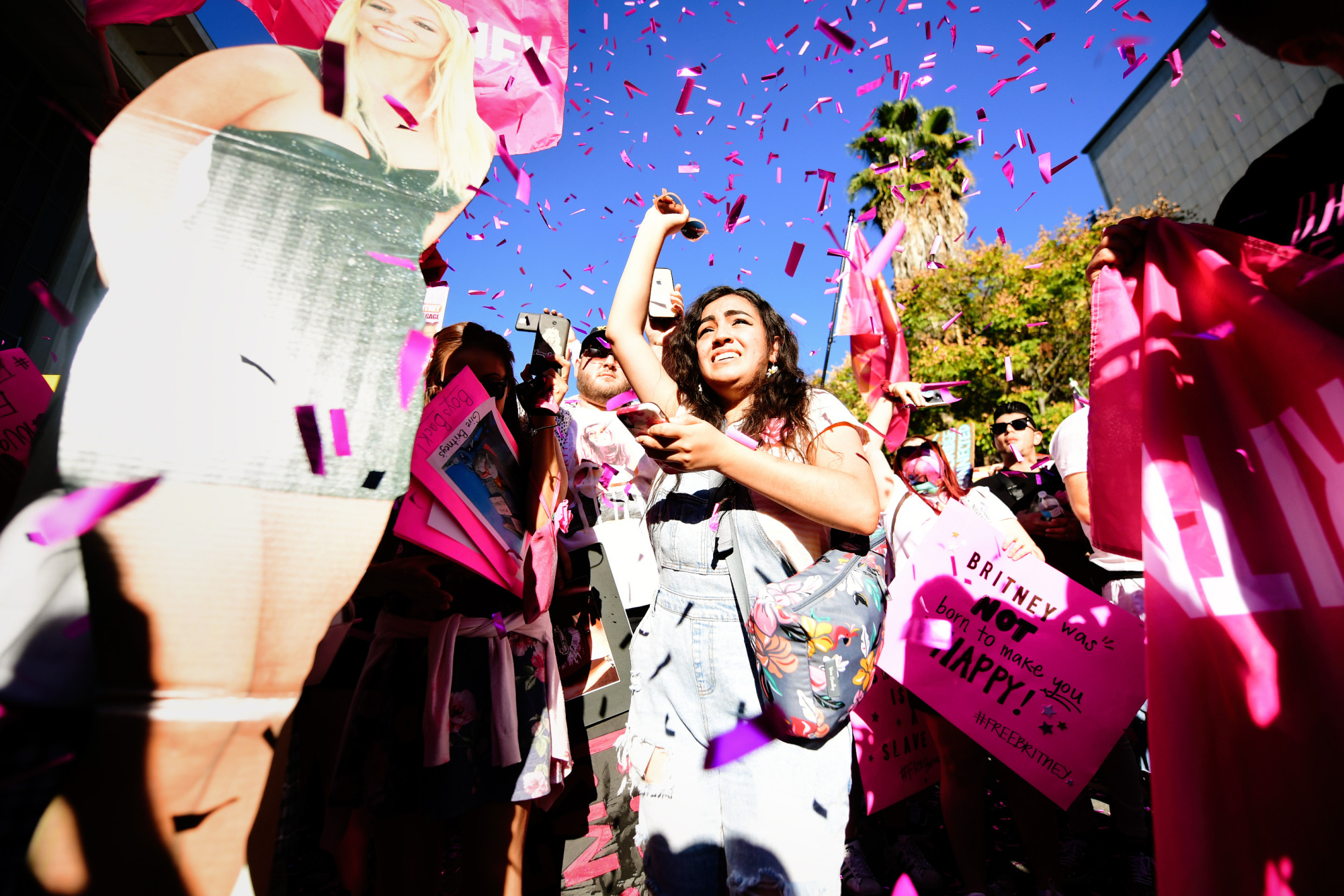 A young woman stands in a crowd of people as pink confetti rains down on her.