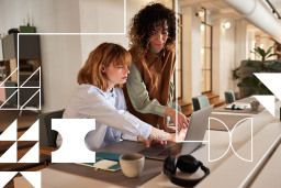 two women pointing at a computer screen with graphic designs and shapes over it