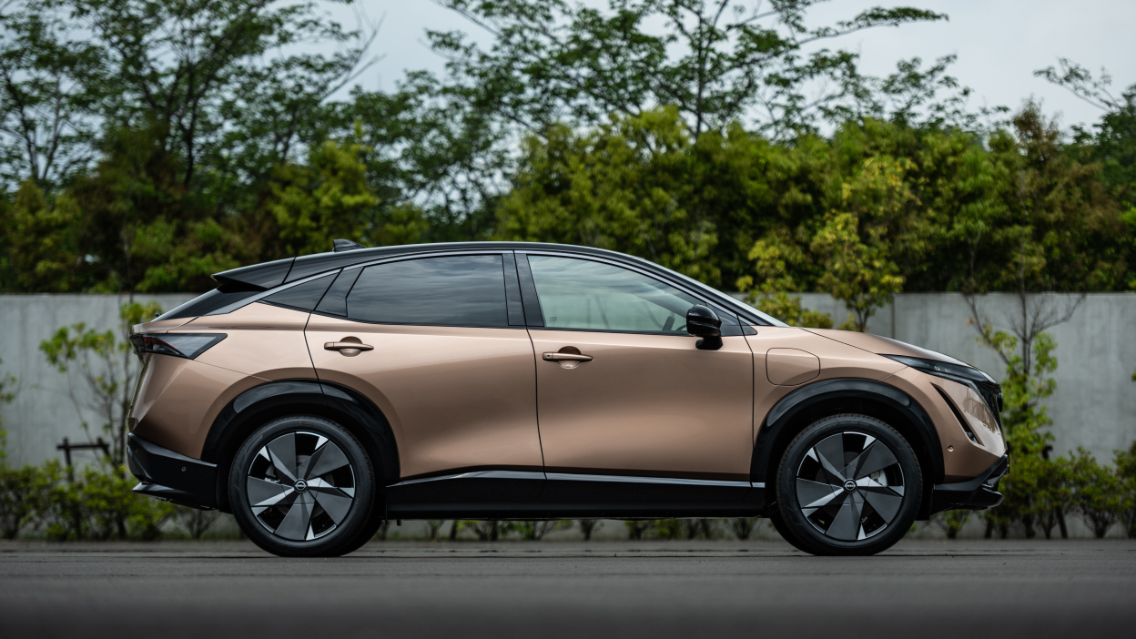A shiny car is parked in front of a fence and trees.