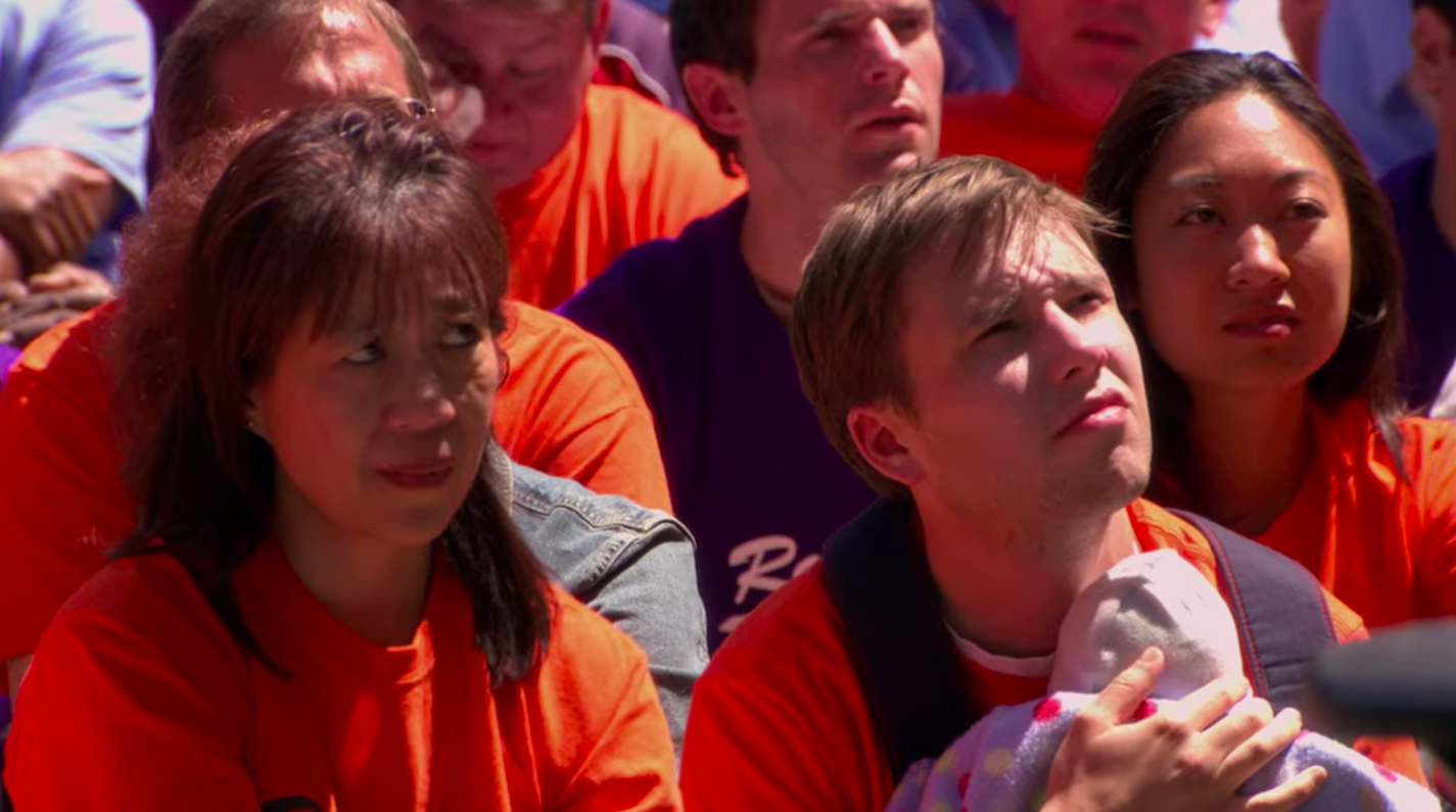 A crowd of extras (including a woman, OfficeTally creator Jennie Tan) wearing orange shirts and sitting on the grass in the "Company Picnic" episode of "The Office."