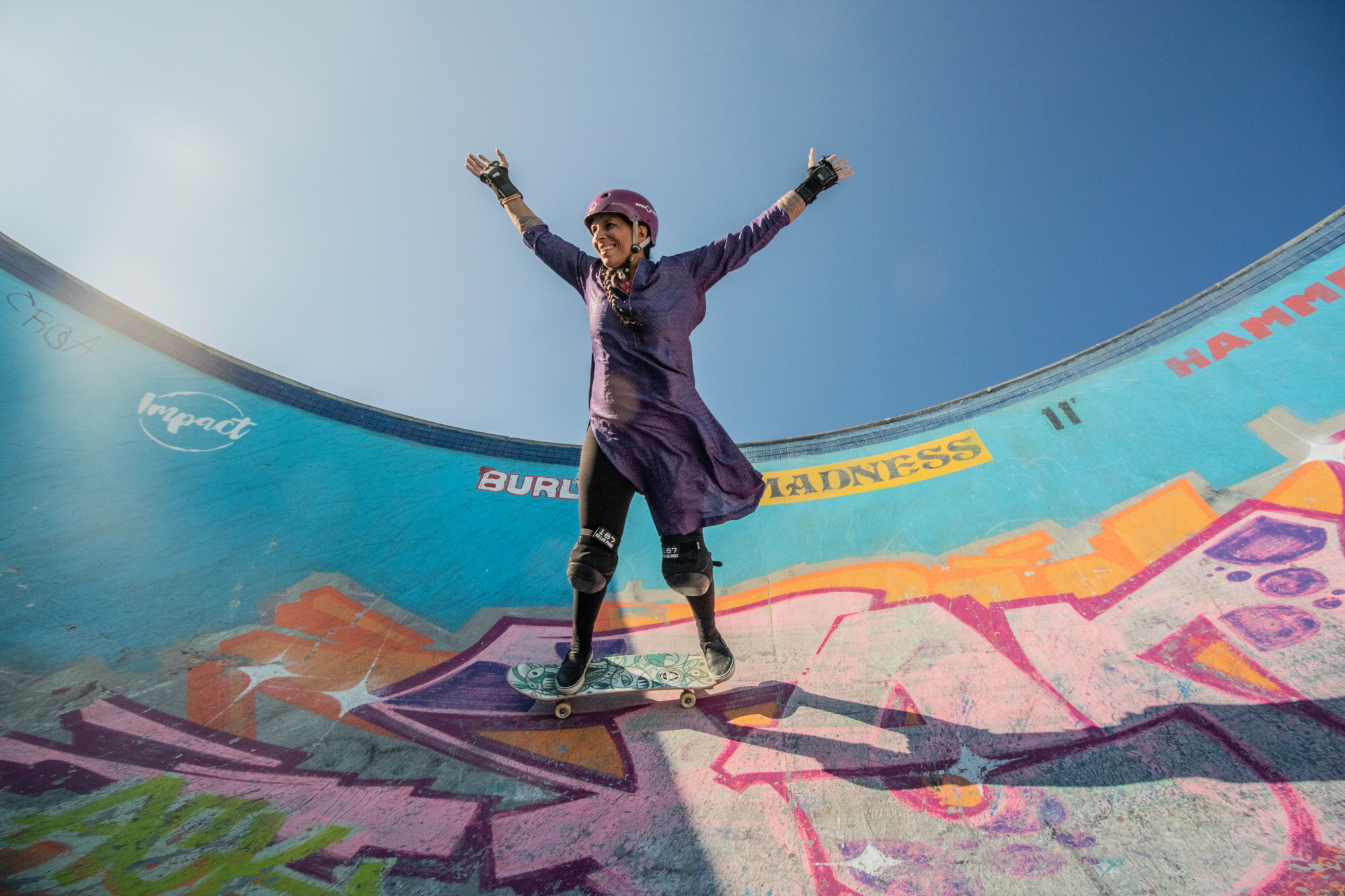 A photo of Roy holding up her arms as she skates inside a half pipe painted in bright colors and graffiti.