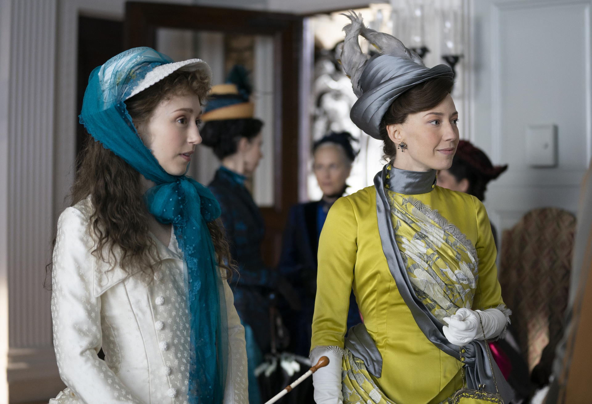 A stylish woman in a yellow 19th century silk dress standing next to a younger girl in a white dress.
