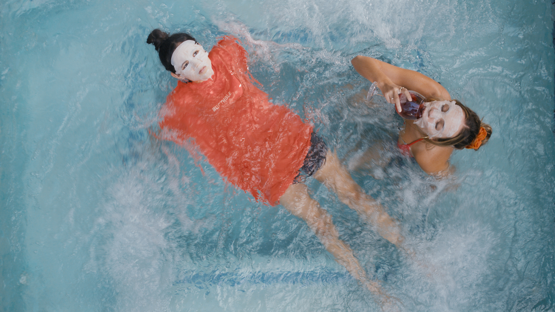 Two teen girls in a jacuzzi, wearing facial masks.