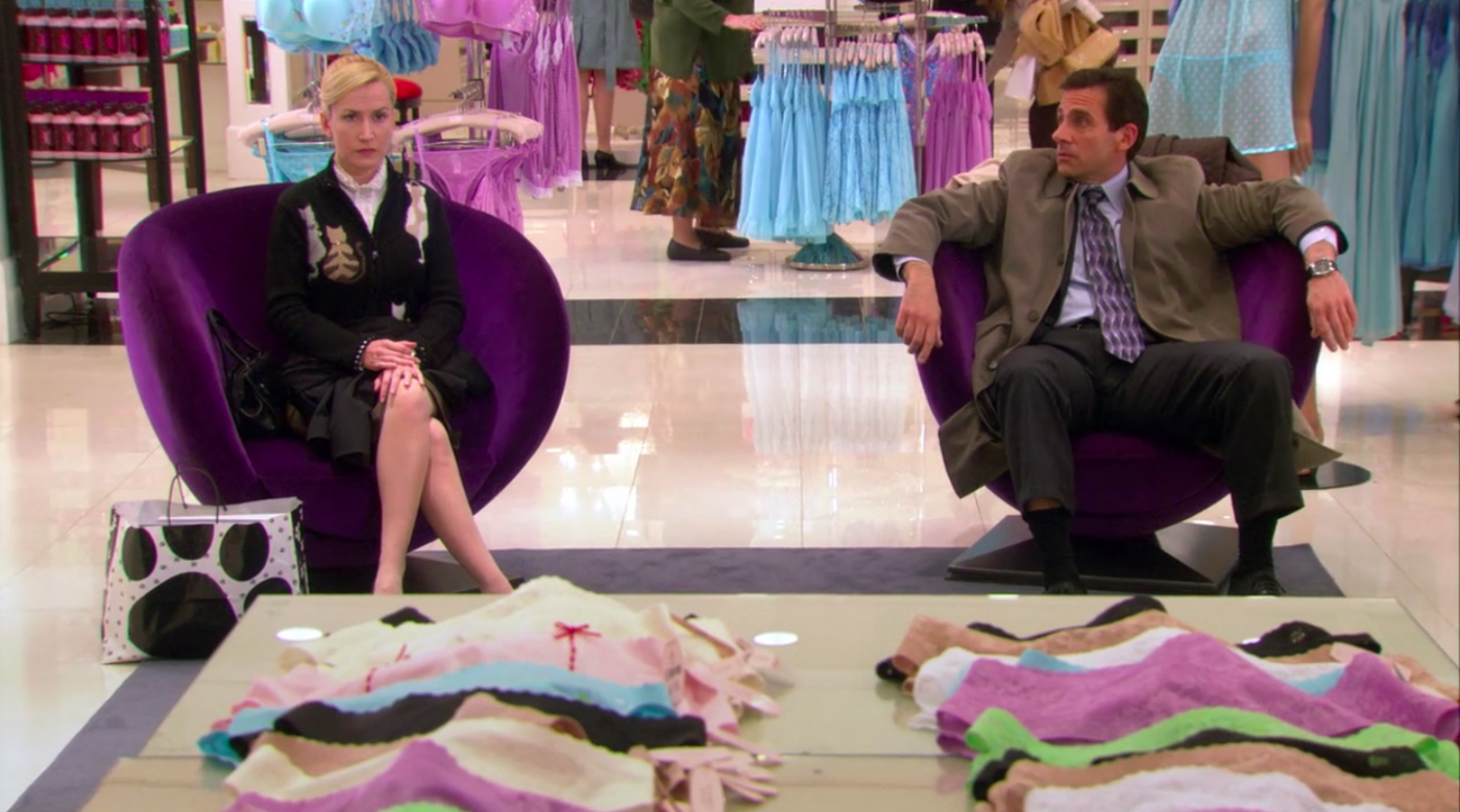 A woman (Angela Kinsey who plays Angela Martin on "The Office") and a man (Steve Carell who plays Michael Scott) sitting in chairs in a Victoria's Secret store.