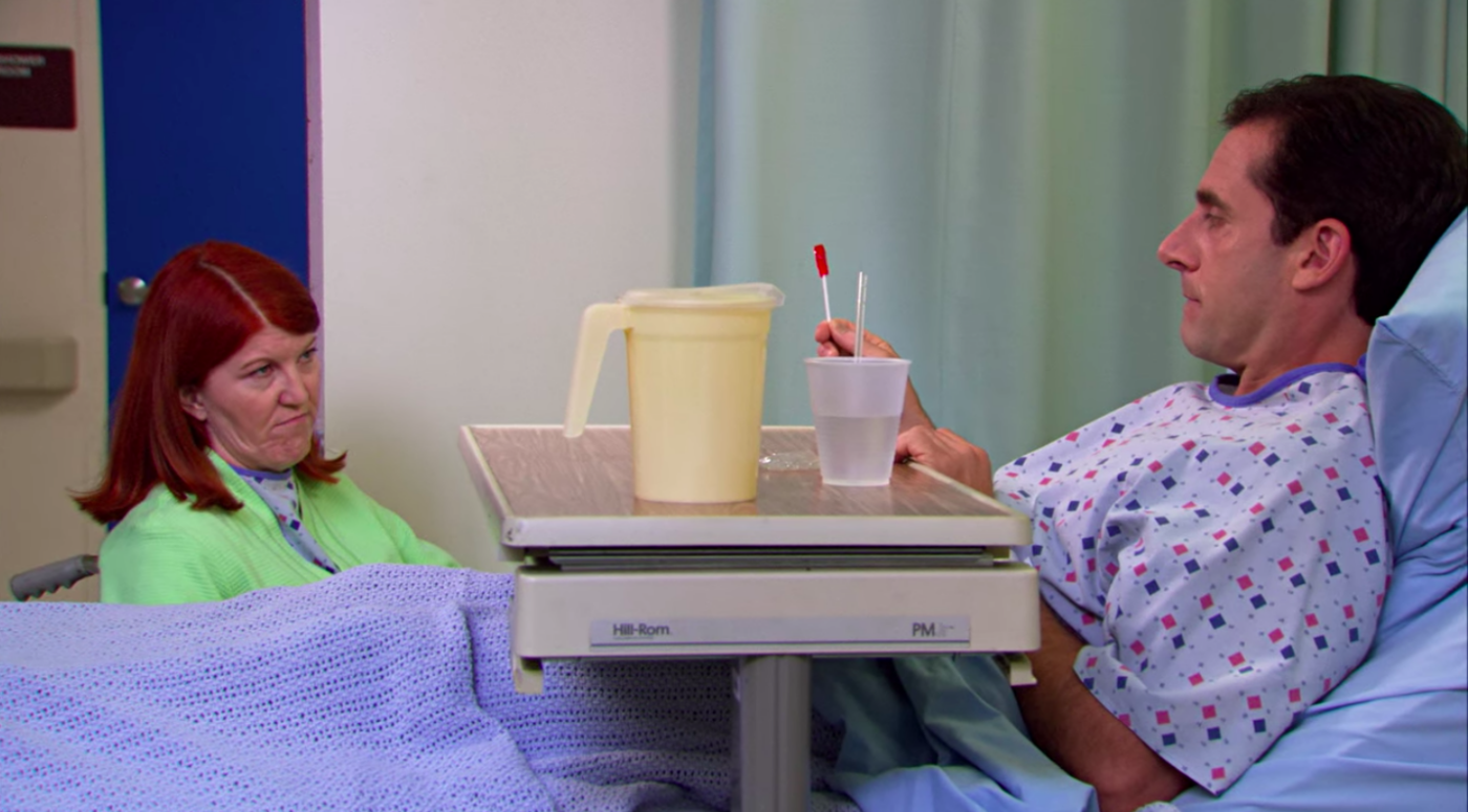 A woman, Kate Flannery (who plays Meredith on The Office), and a man, Steve Carell (who plays Michael Scott), sharing a red lollipop in a hospital room.