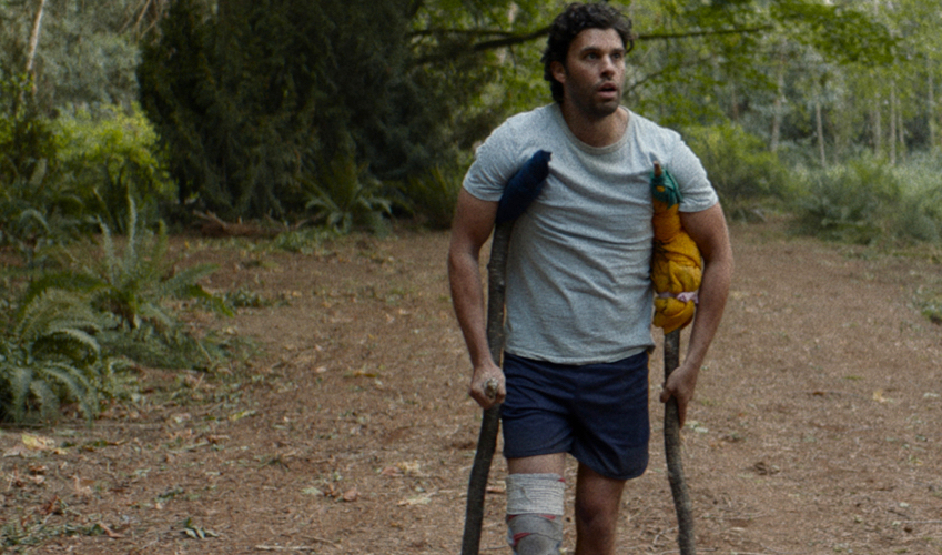 A man walks through the woods on crutches with a bandaged leg.
