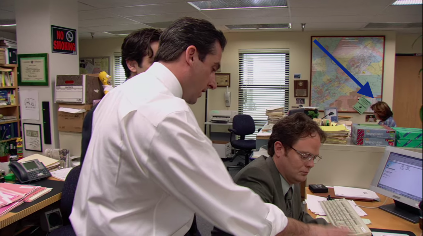Several cast members of "The Office" in an episode with an arrow pointing to a background actor.