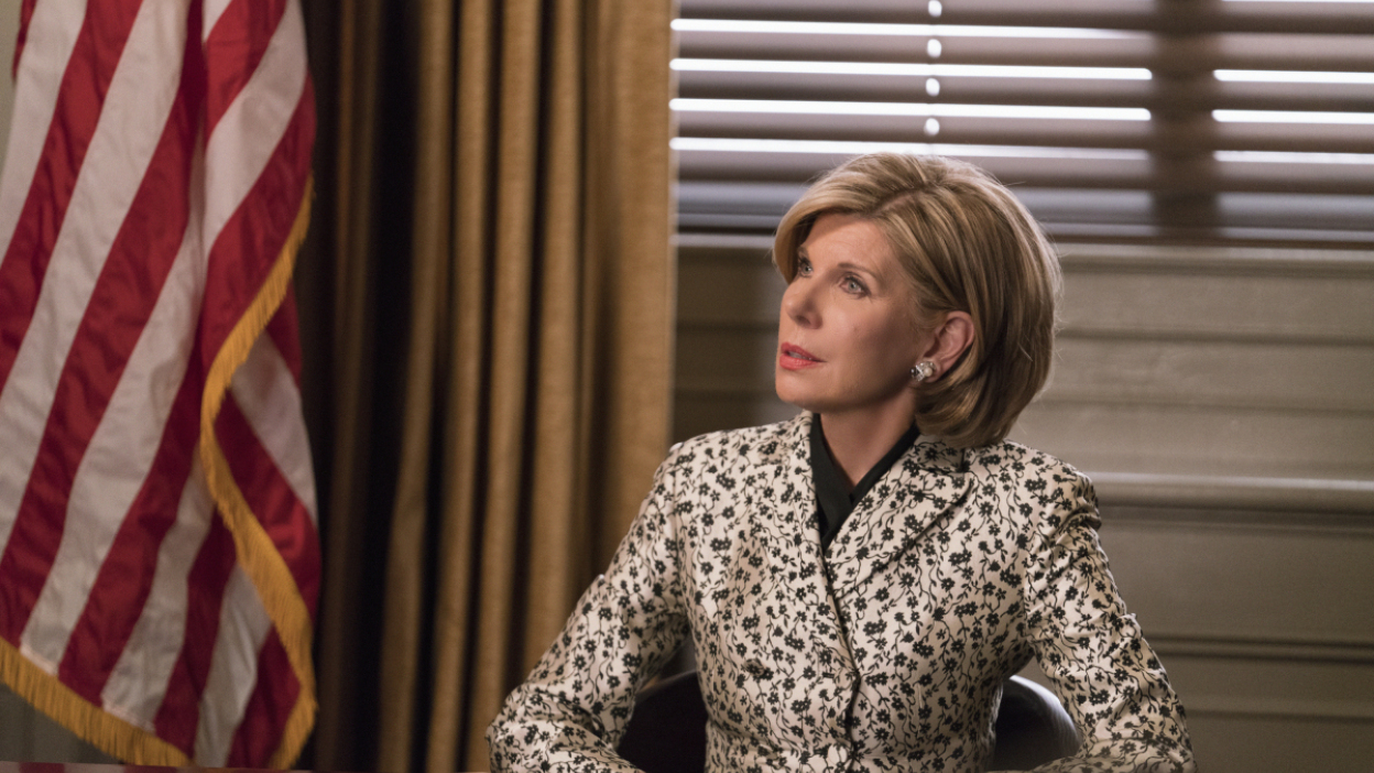 A seated woman in a gold blazer, with the American flag off to the side.