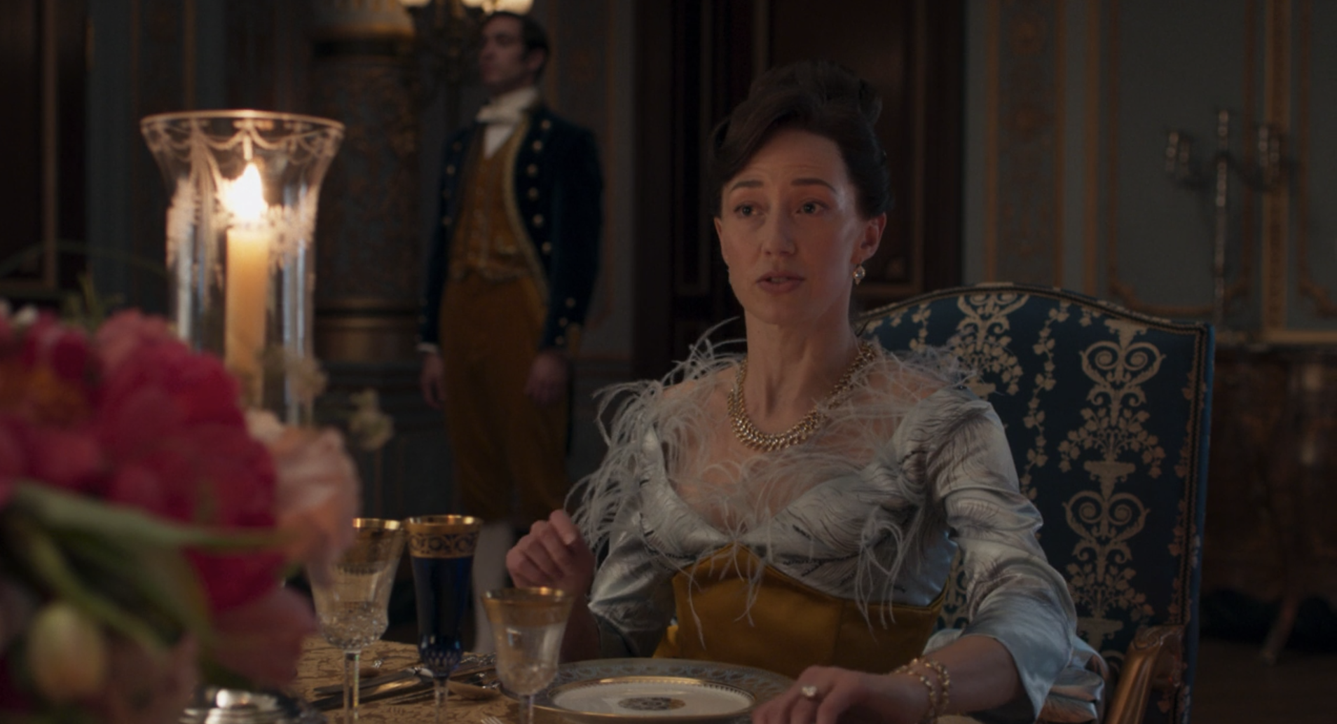 A dark-haired woman wearing a blue satin dress with long, fluffy feathers sprouting from the bodice.