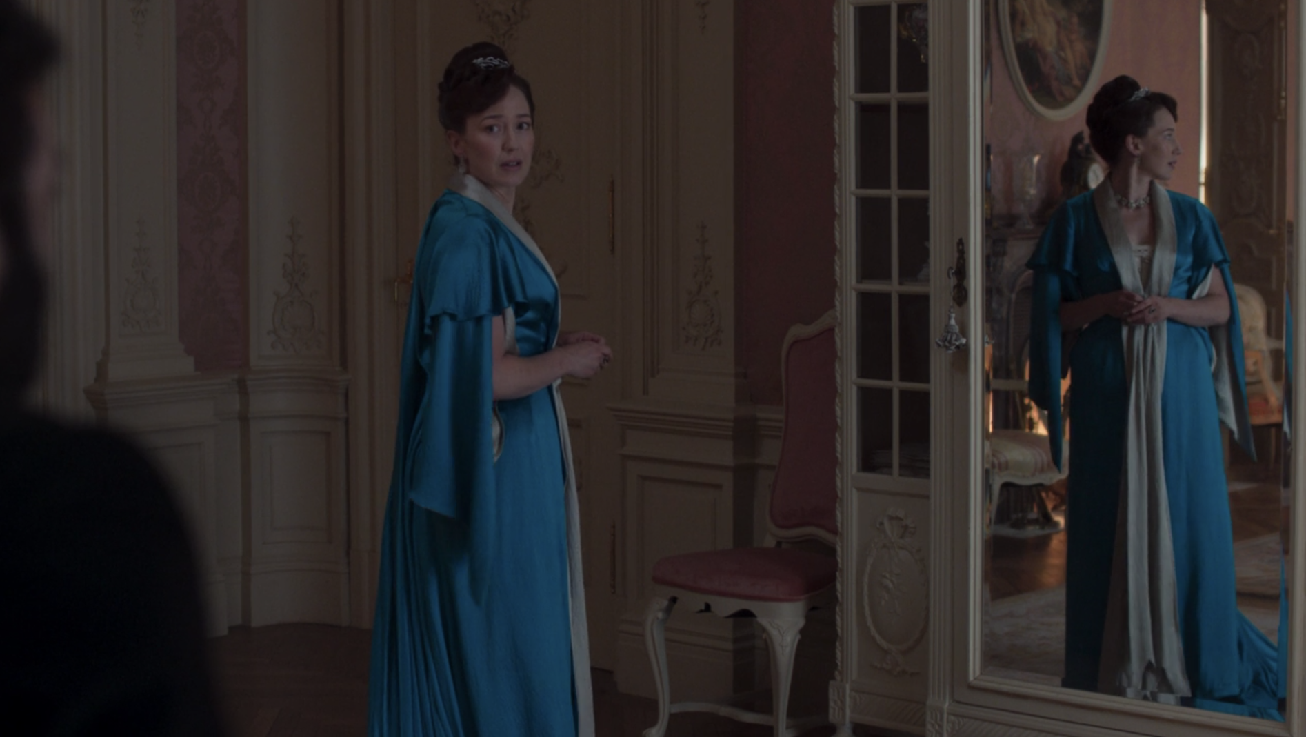A haired woman with a diamond tiara wearing a cobalt blue, floor length dressing gown.