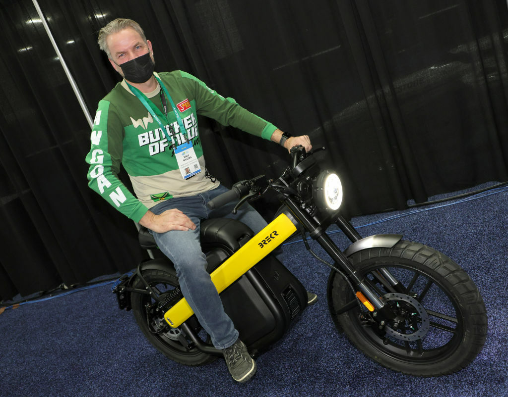 A man in a green zip-up and black mask poses on a bike inside.