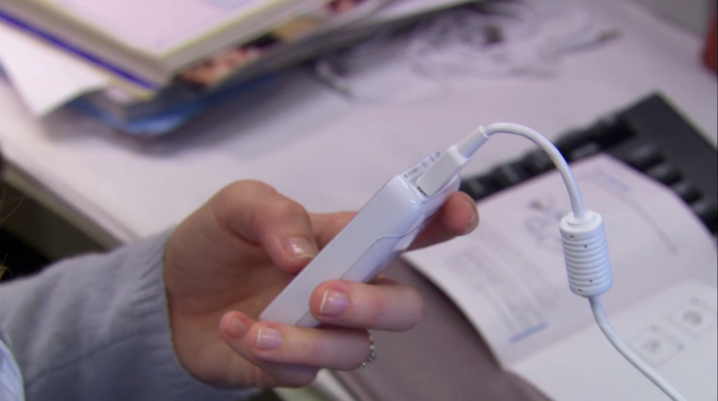 A hand holding a small white tech device.