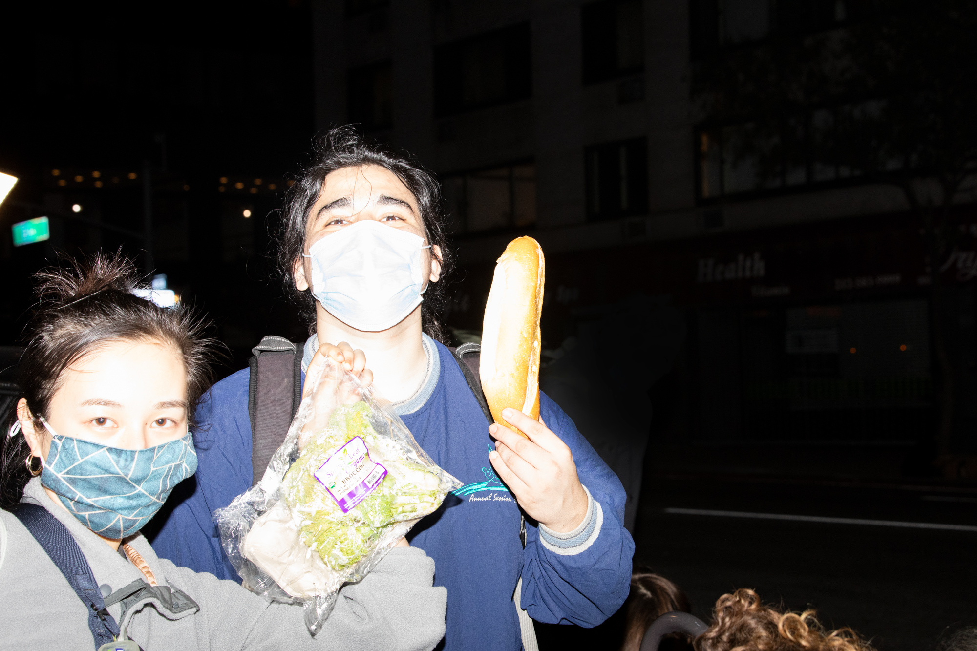 two freegans holding up a loaf of bread and bag of broccoli 