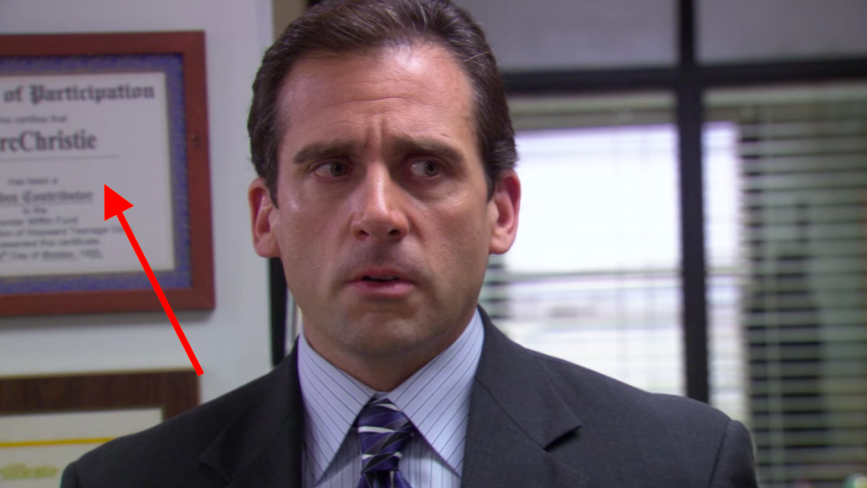 A man, Steve Carell (who plays Michael Scott on "The Office"), standing in front of a plaque that's hanging on a wall..