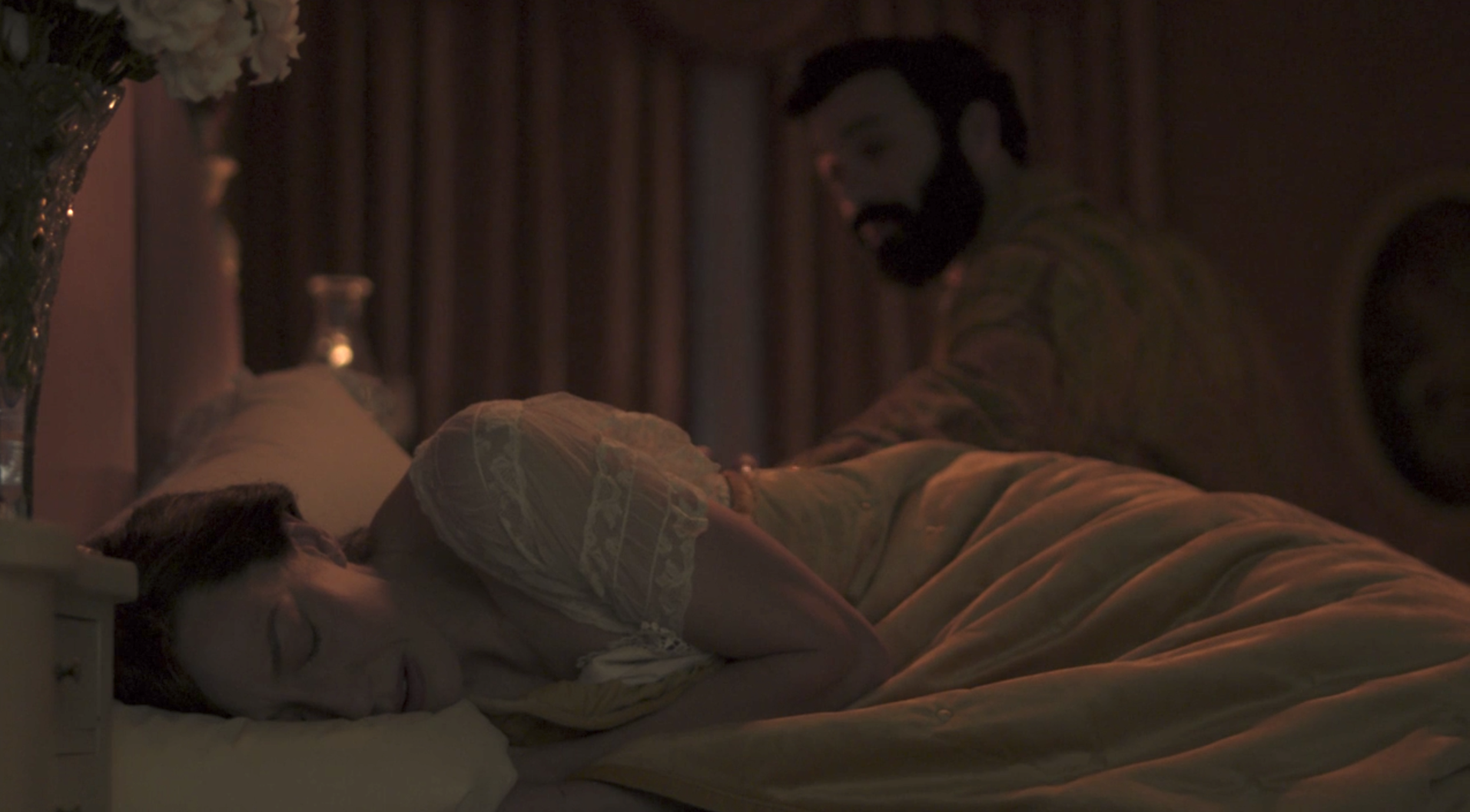 A woman laying in a large bed and crying. She is wearing a white nightgown with short lace sleeves.