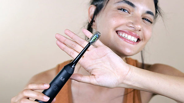 Person smiling and holding black toothbrush up to camera