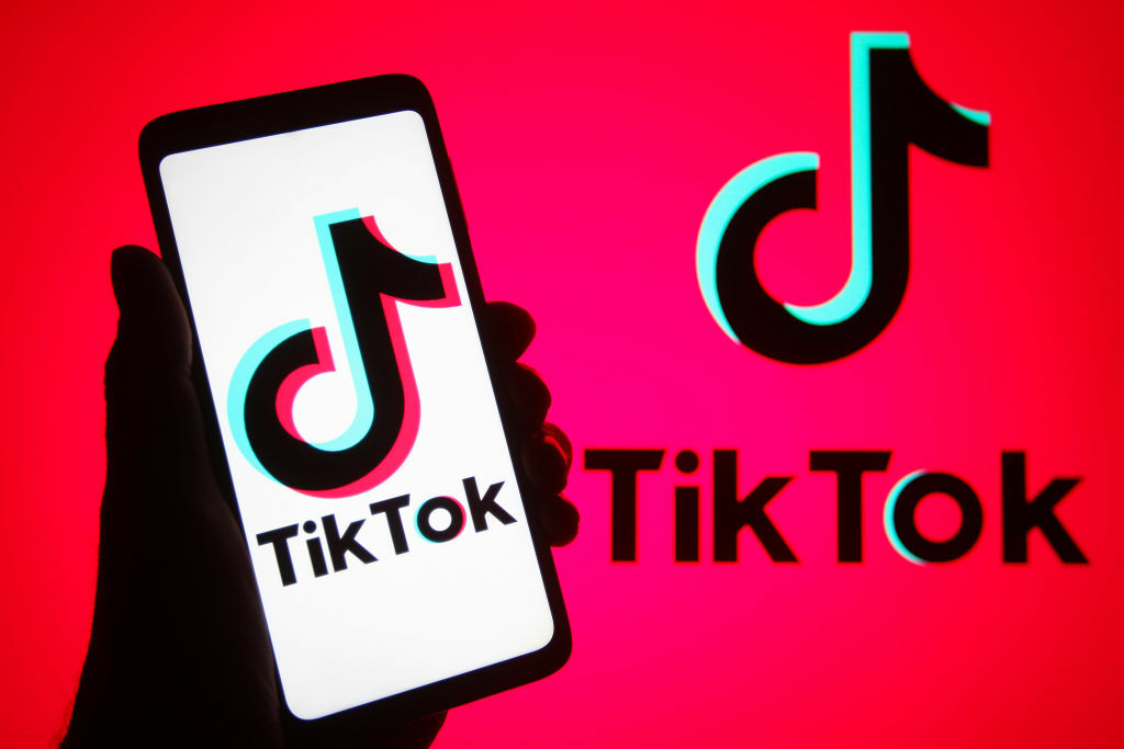 The TikTok logo on a smartphone and on a red background.