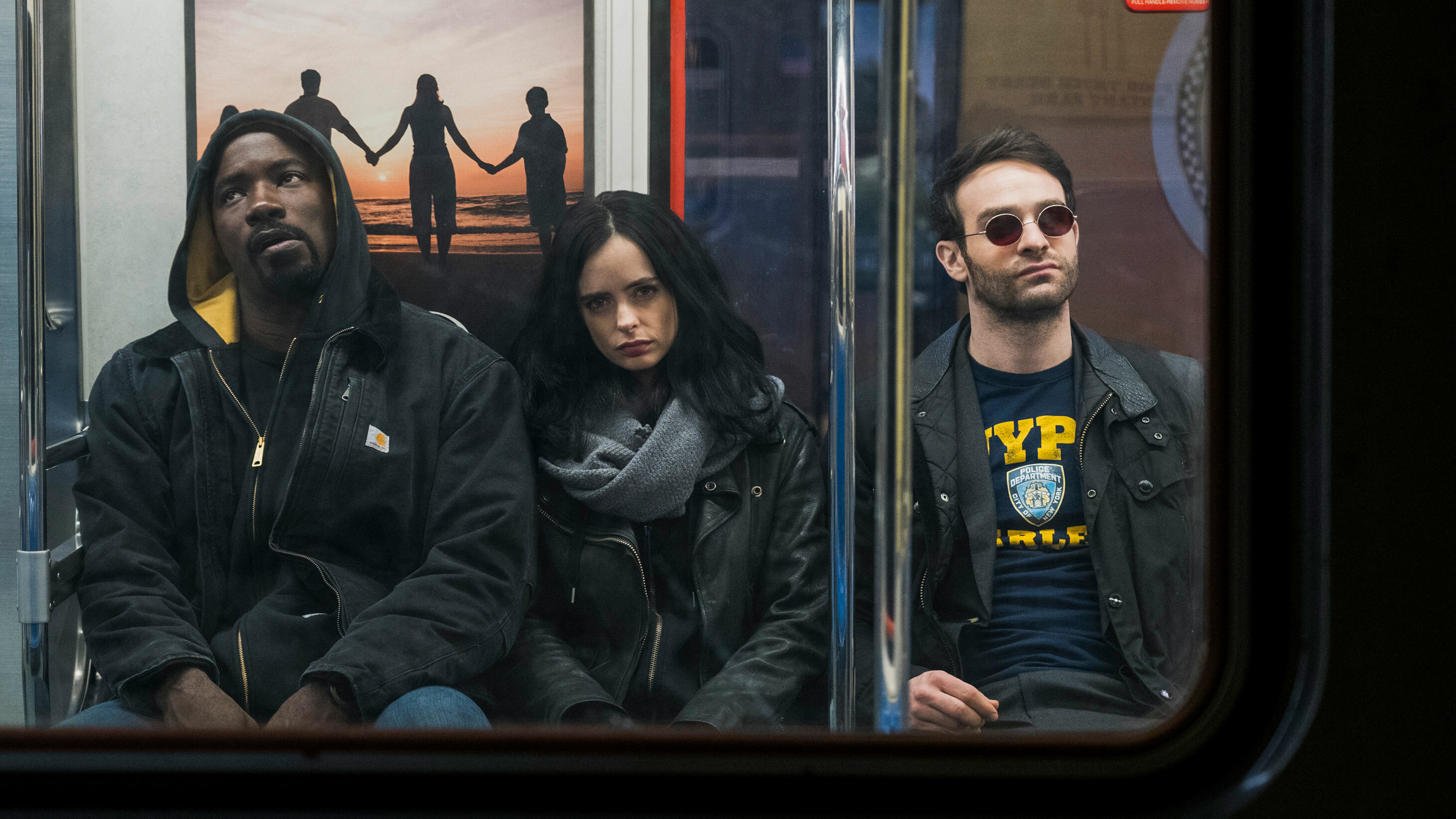 A still from 'Marvel's Defenders' on Netflix. Three people sit side-by-side in a subway, viewed through one of the subway car's windows.