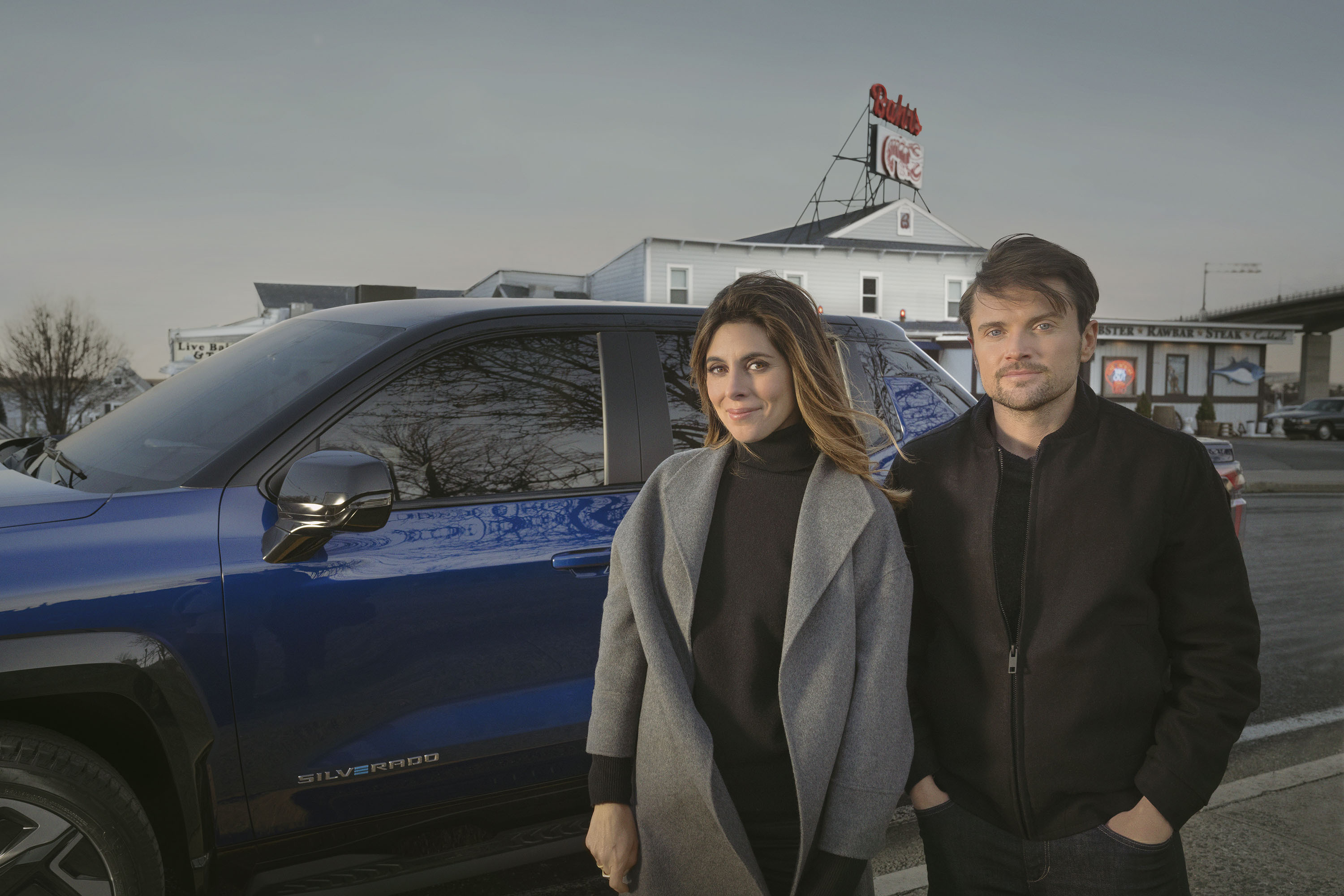 Jamie-Lynn Sigler and Robert Iler stand in front of the Silverado electric truck in blue.