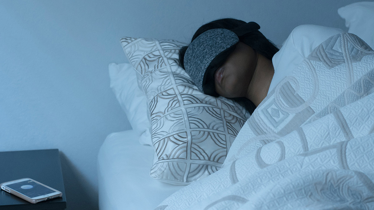 Person sleeping in bed wearing grey sleeping mask