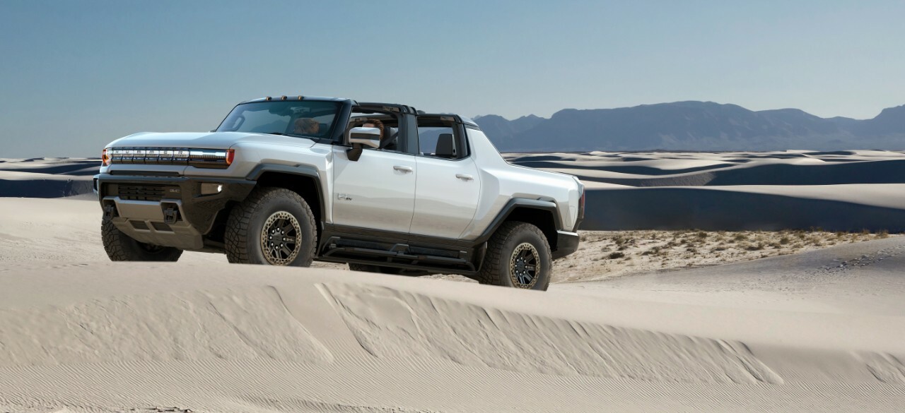 A white Hummer EV truck driving through sand dunes.