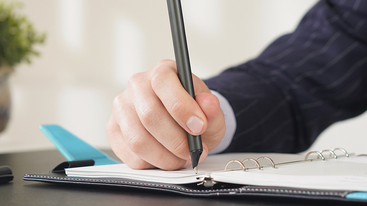 Hand writing in notebook with grey pen
