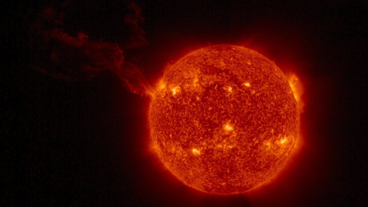 A look at the sun, with a large plume of plasma visibly erupting in a wide, looping arc in the top left quadrant of the image.