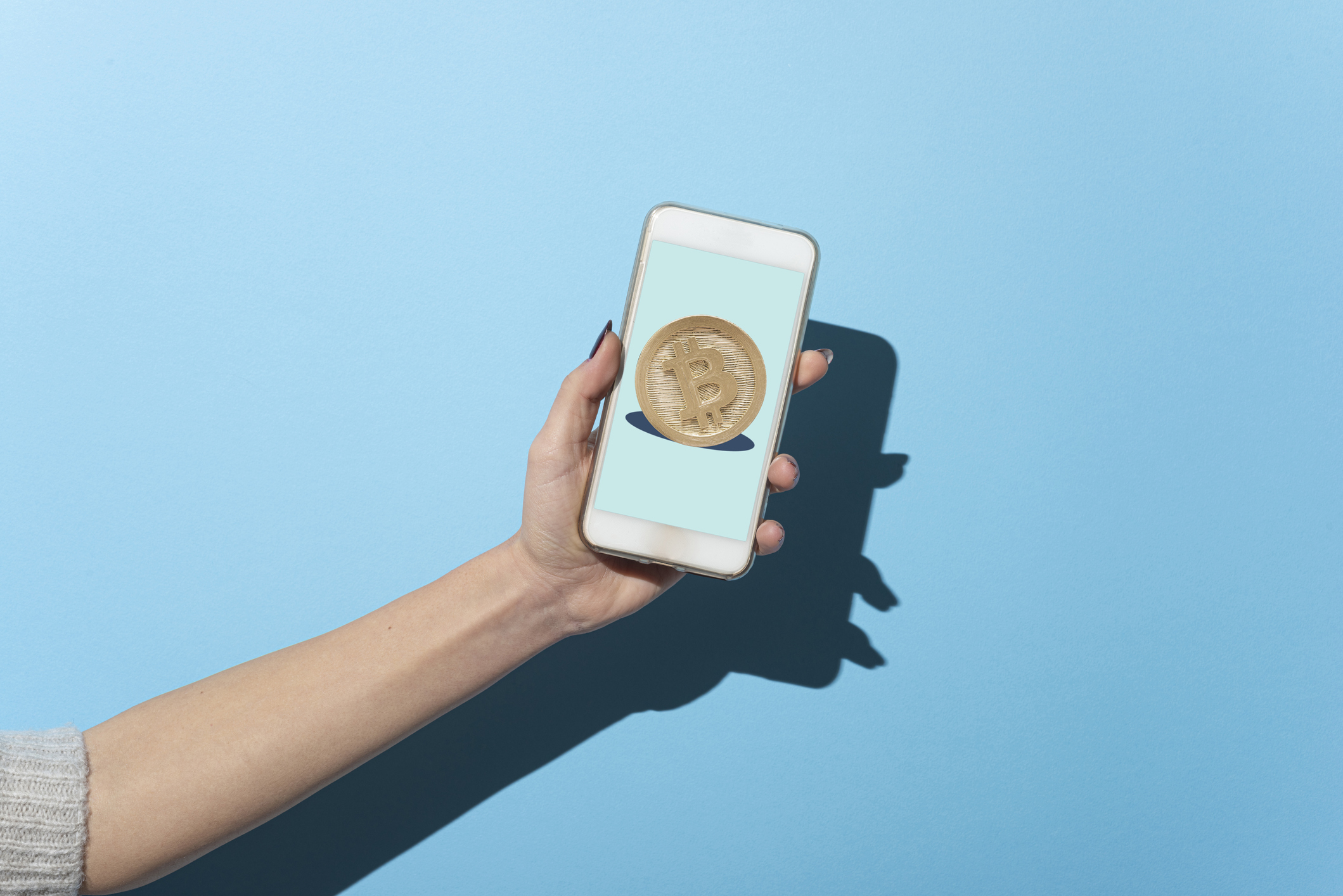 Woman holding a smartpone with a photo of the Bitcoin logo.