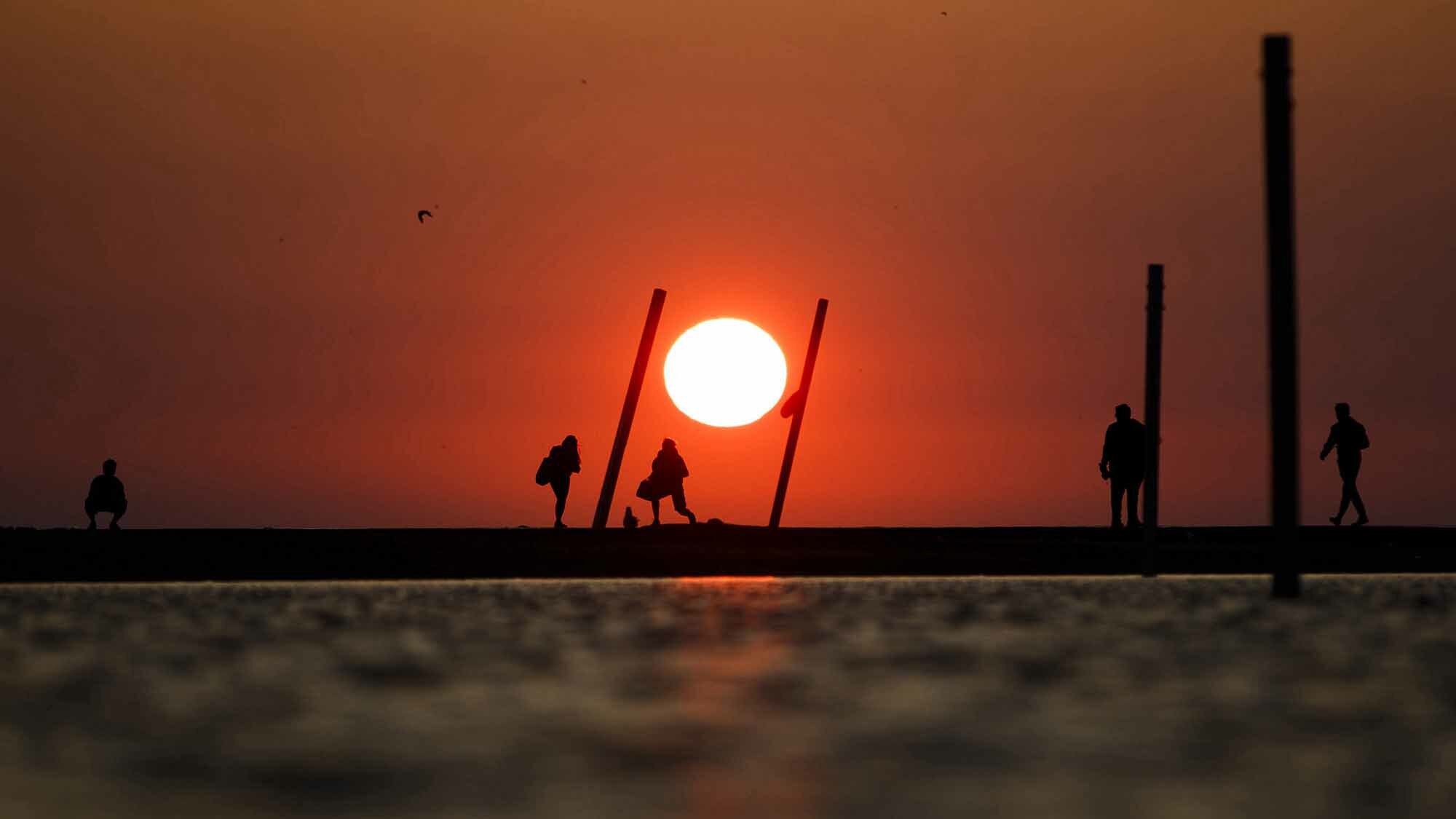 A bright orange sun sits in the horizon above Lake Michigan on a hot day in Chicago.