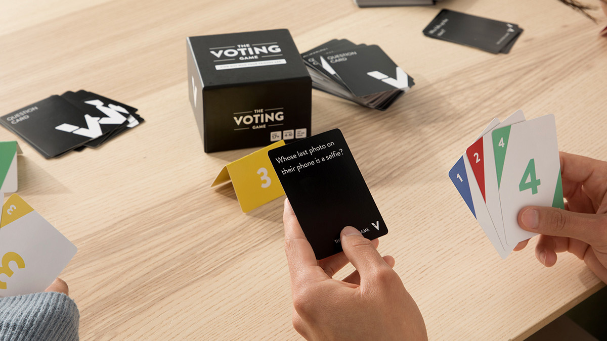 Hands holding cards from the voting game, with more cards and box on wooden table