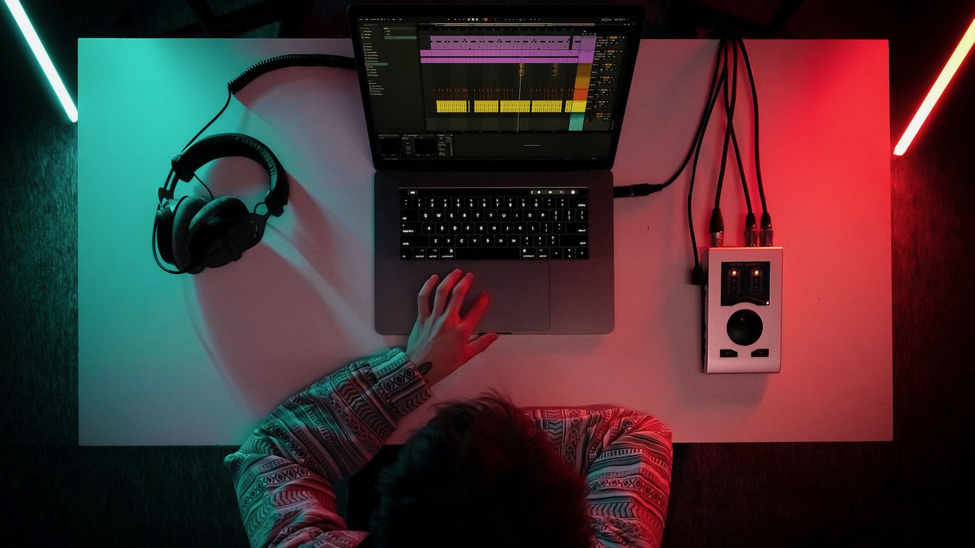 Bird's eye view of person using laptop connected to sound equipment, with sound editing software window on screen
