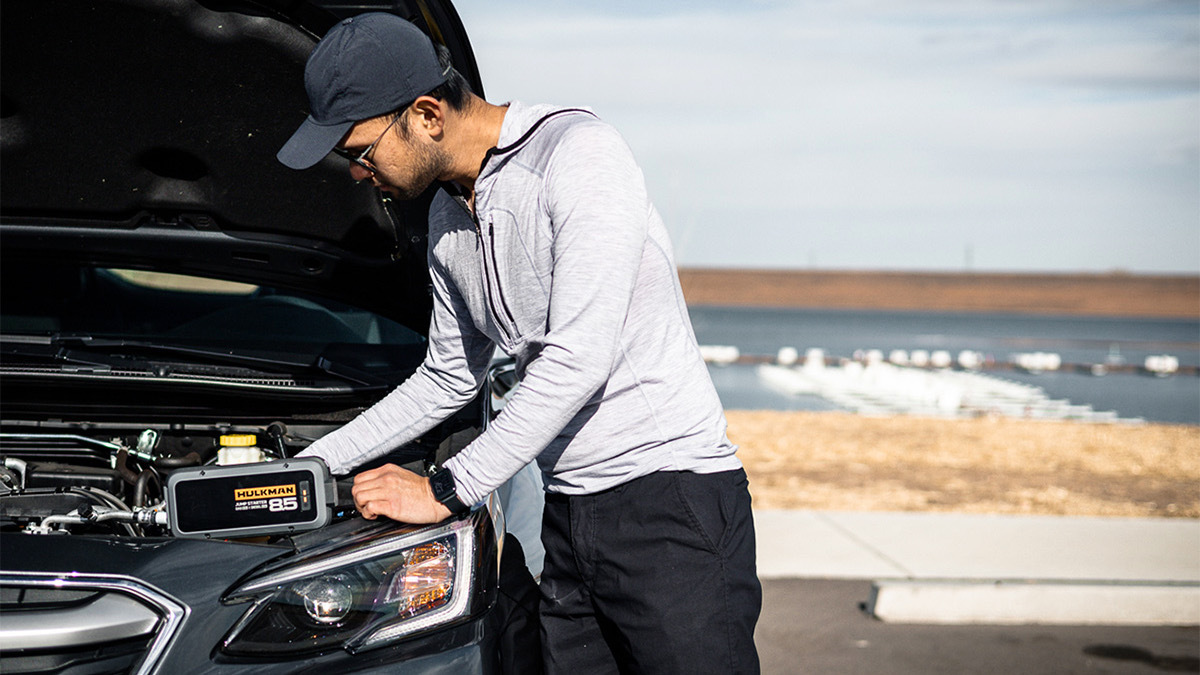 Person jumpstarting car with hood up