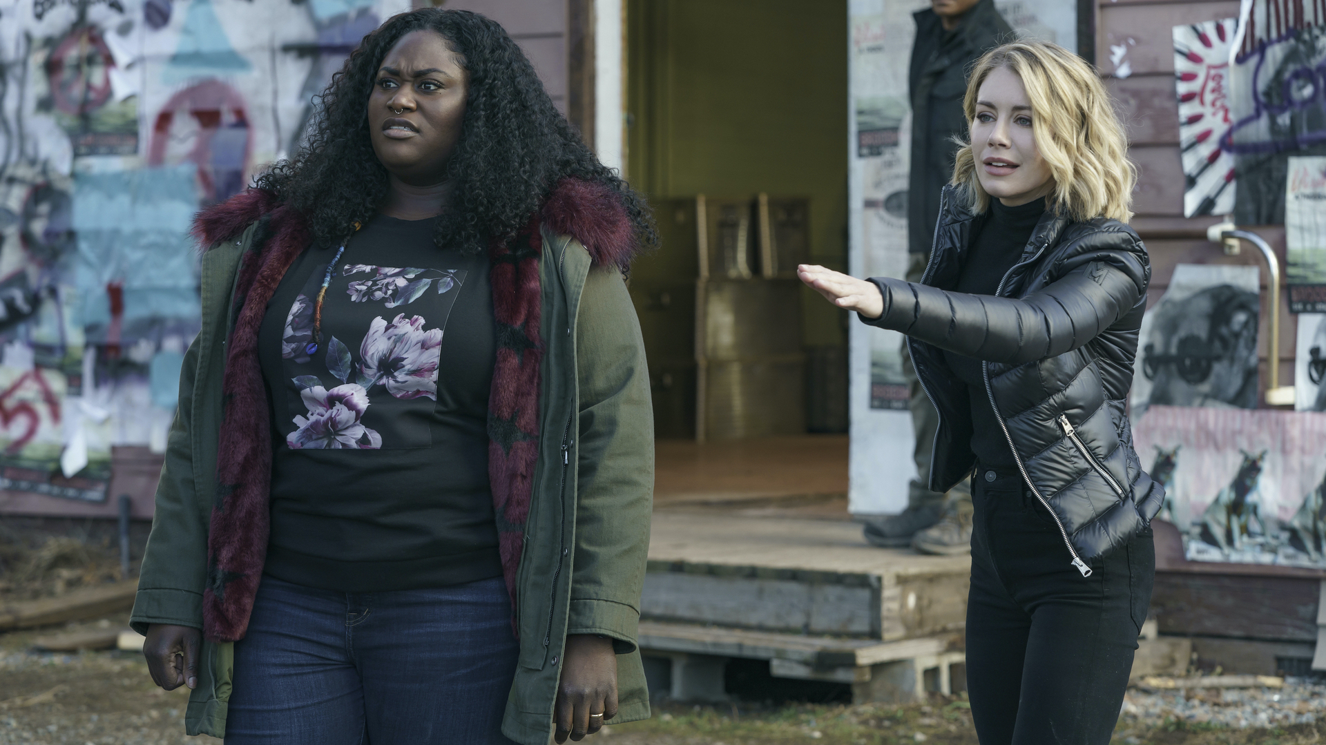 Two women outside a building, one with her hand out as if asking someone to stop; a still from "Peacemaker."