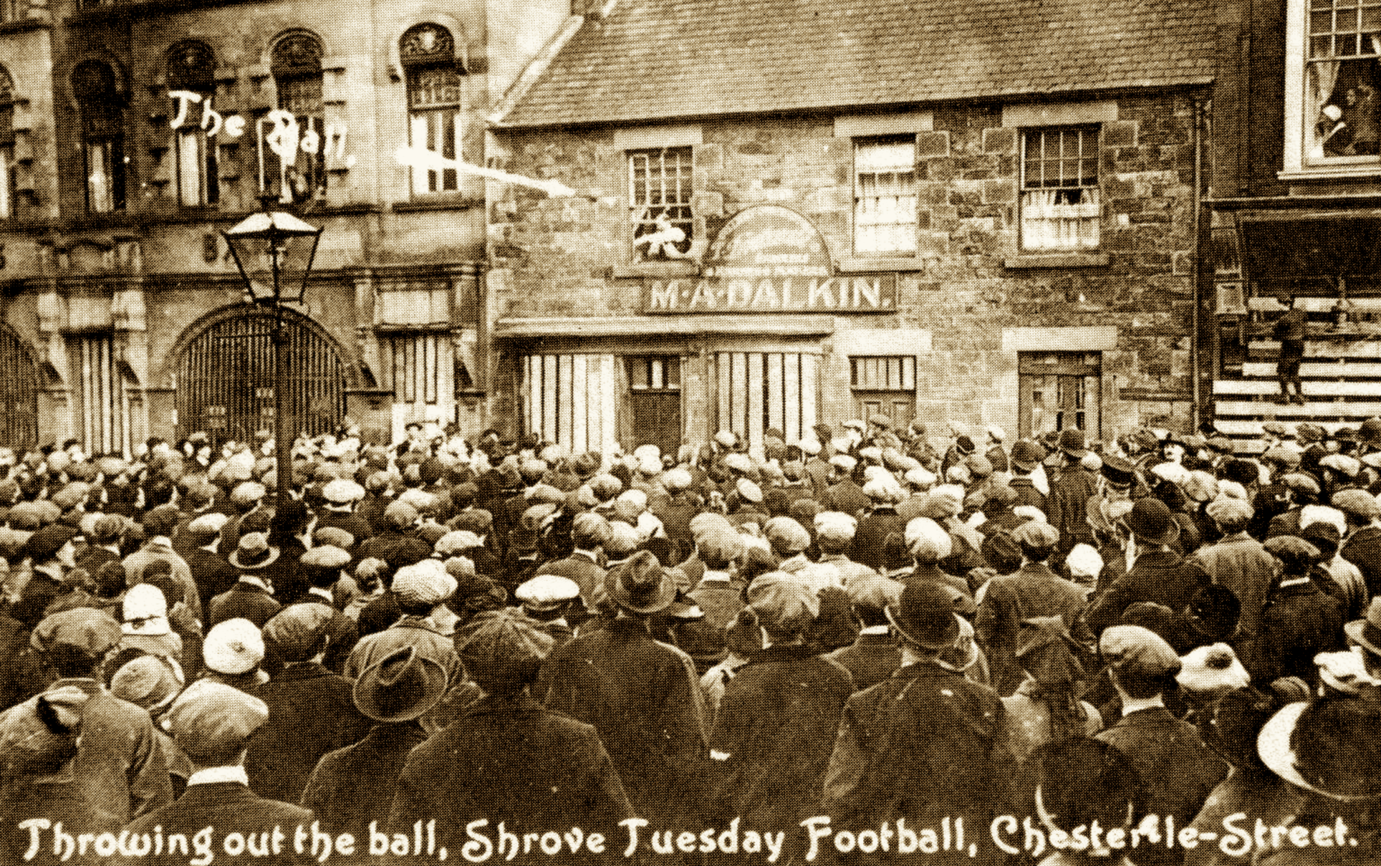 A sepia photograph of a man in a shop window throwing a ball out to the crowd.