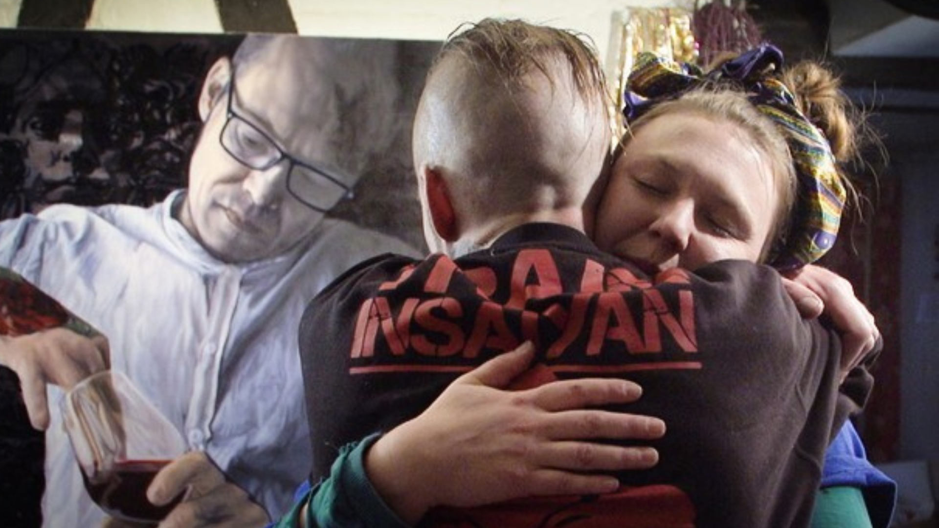 A man hugs a woman in front of a painting.