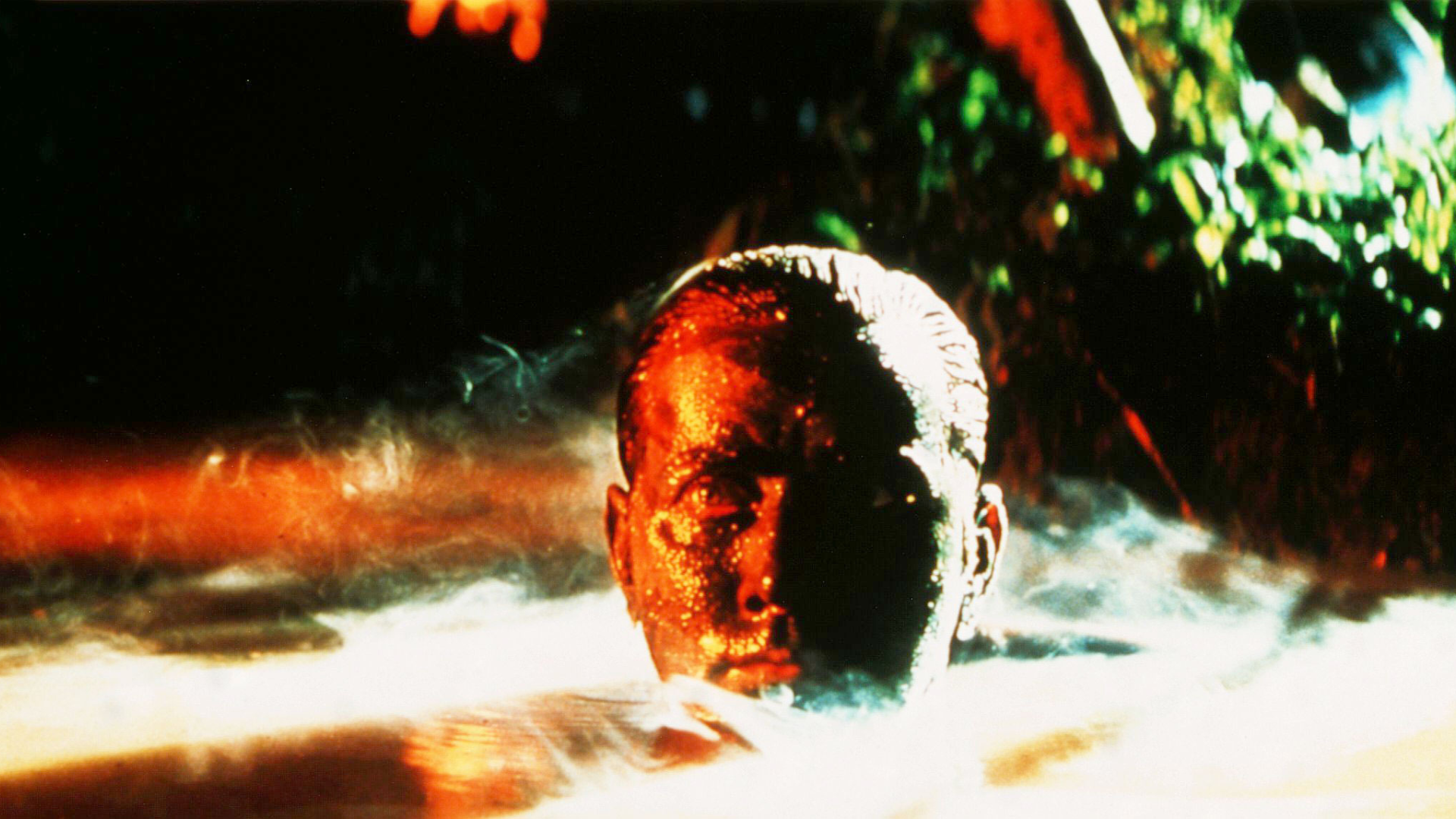 A white man with war paint on his face peeks out of a lagoon.