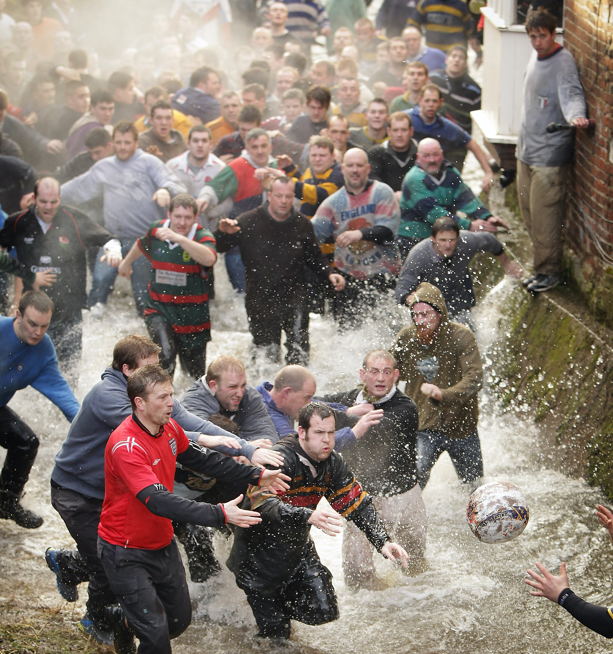 Dozens of men chase a ball through a shallow stream