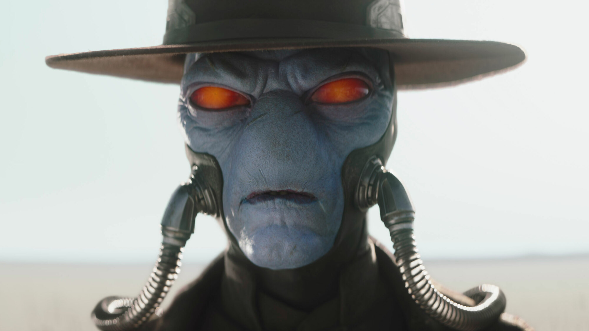 A close-up of a blue-skinned alien's face. He has red eyes, a slit for a mouth, and two hoses, apparently breathing tubes, coming out of his cheeks. This is a still from "The Book of Boba Fett" and the character is Cad Bane.