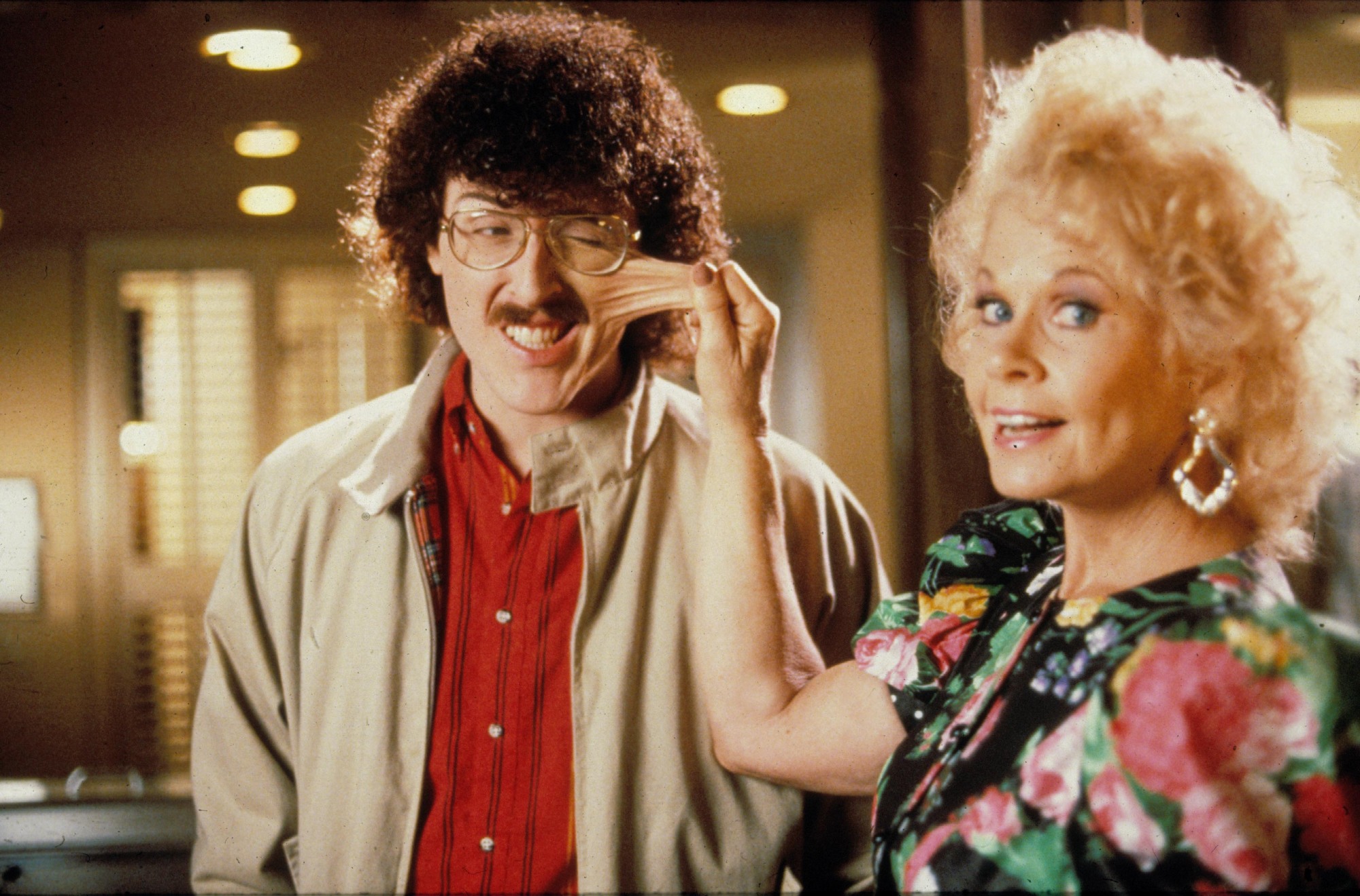 A still from UHF, showing Weird Al Yankovic with a prosthetic cheek being pinched,