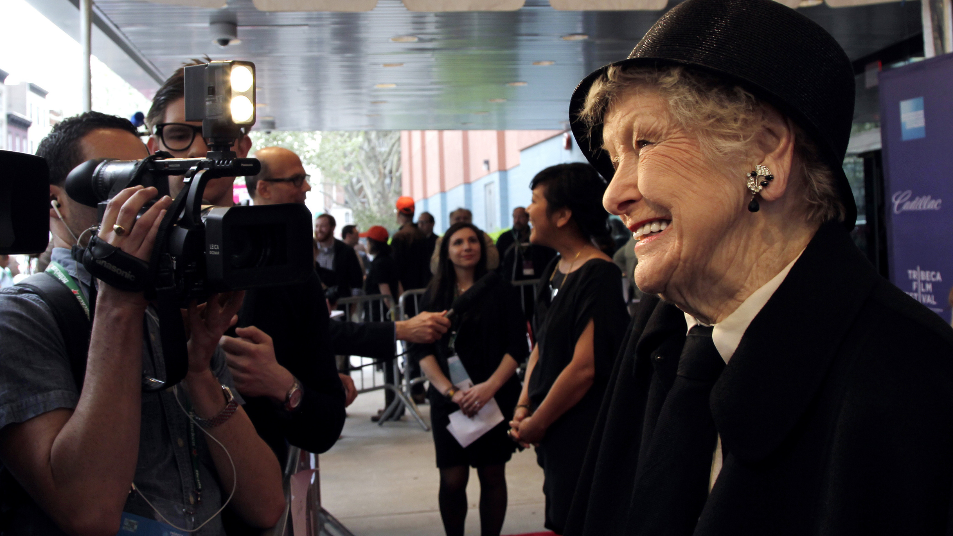 A classy old woman stands in front of photographers at a red carpet event.