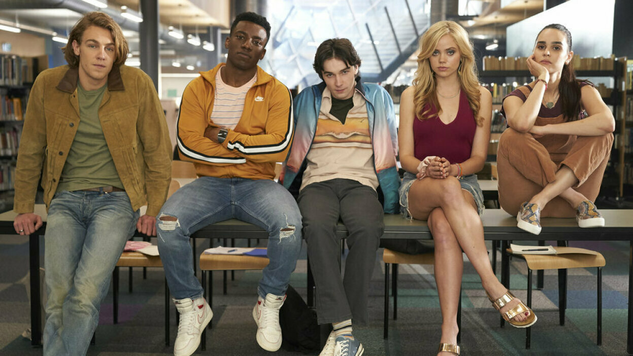 Teenagers sit on a library table, looking bored. 