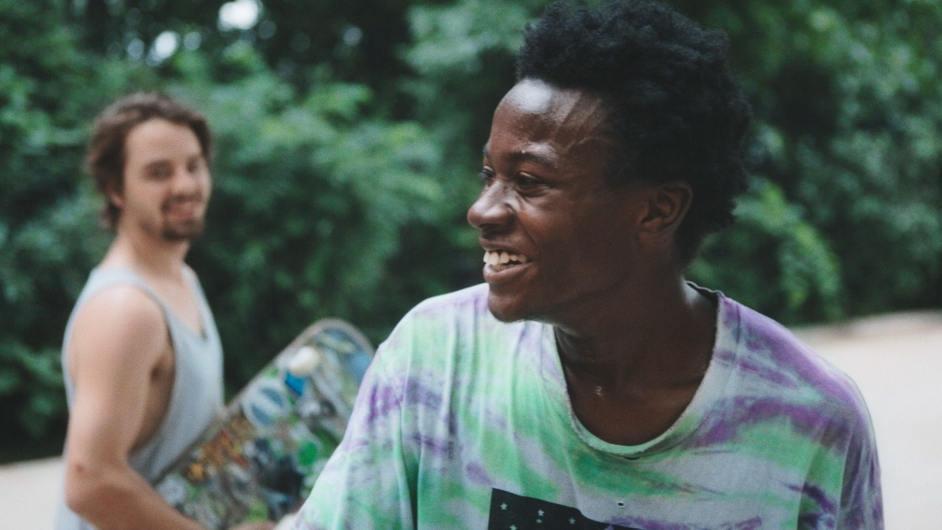 Two young men smile with their skateboards in hand.