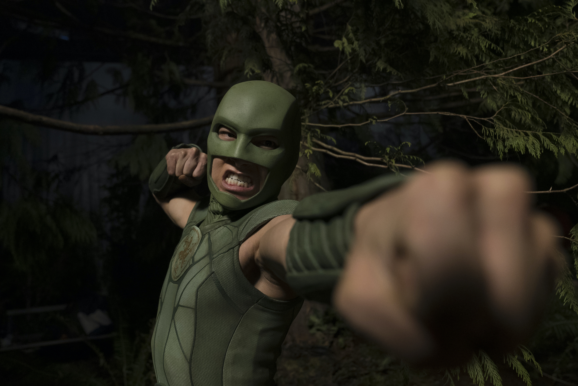 A person in a green mask and bodysuit, ready for combat; a still from "Peacemaker."