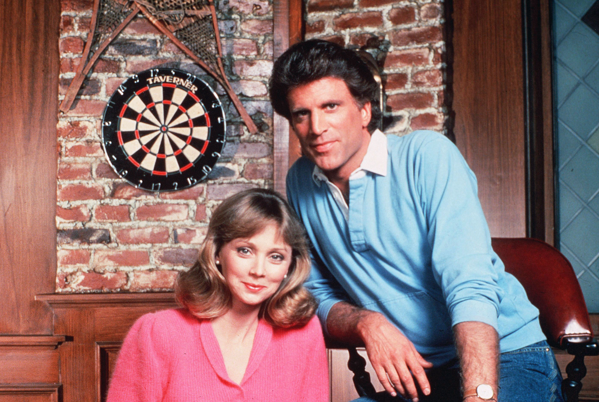A handsome man and a beautiful woman pose in a bar. 