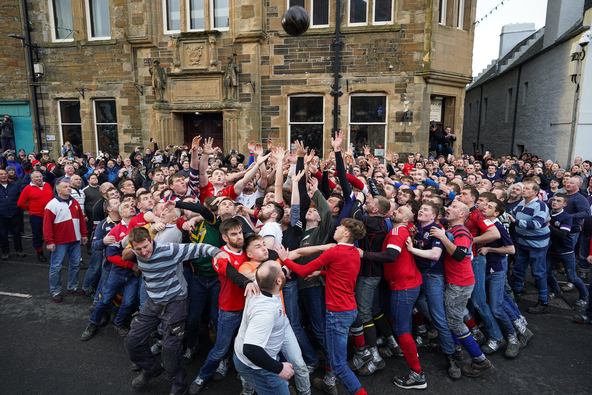 A large group of men jostle for a ball outside a town hall.