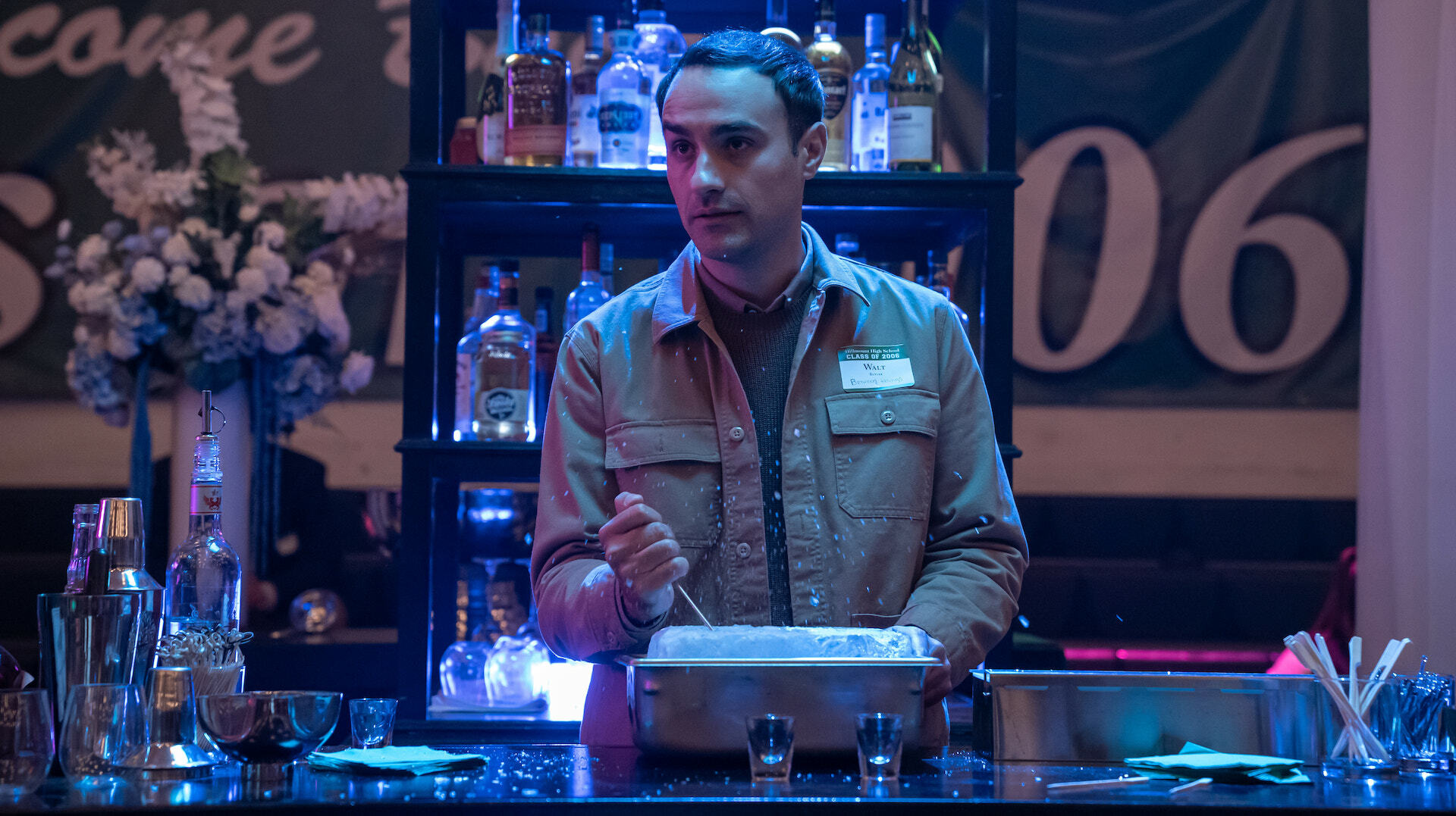 A man breaks ice behind the bar at a high school reunion in the gym; a still from "The Afterparty."