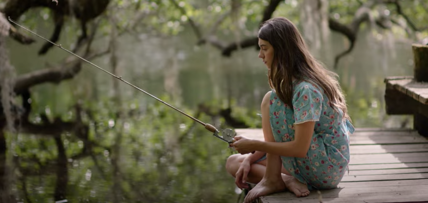 A still from 'Where The Crawdads Sing', featuring Daisy Edgwar-Jones sitting by the water holding a wishing rod.